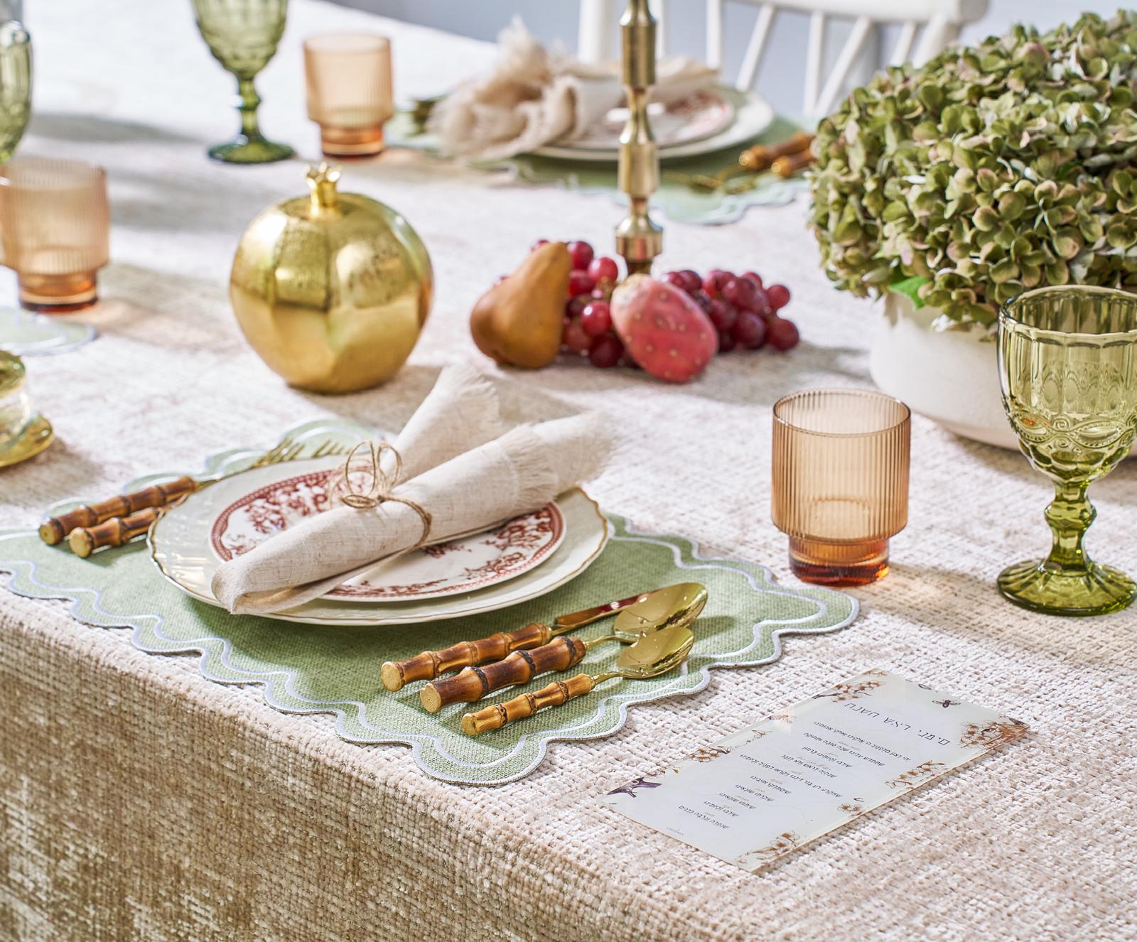 Holiday table with green scalloped placemats, amber tumblers, green stemware, and gold accents